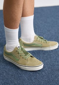 Baskets en daim vert avec des lacets assortis, semelle en caoutchouc blanc et accents vert foncé. Portées avec des chaussettes blanches à côtes.