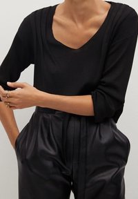 Haut noir en maille côtelée avec un col en V et des manches trois-quarts, associé à un pantalon en cuir noir taille haute avec des plis.