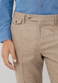 Smešani smeđi hrapavi materijal za hlače s bočnim džepovima i naglascima s gumbima. Nosi se s svijetloplavom košuljom s kragnom na gumbe.