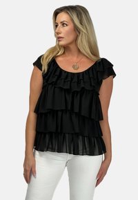 Czarny top z falbanami warstwowymi, z okrągłym dekoltem i krótkimi rękawami, wykonany z lekkiego materiału; zestawiony z białymi spodniami slim-fit.