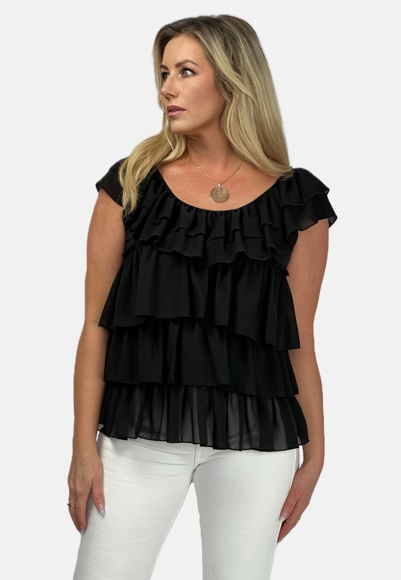 Czarny top z falbanami warstwowymi, z okrągłym dekoltem i krótkimi rękawami, wykonany z lekkiego materiału; zestawiony z białymi spodniami slim-fit.