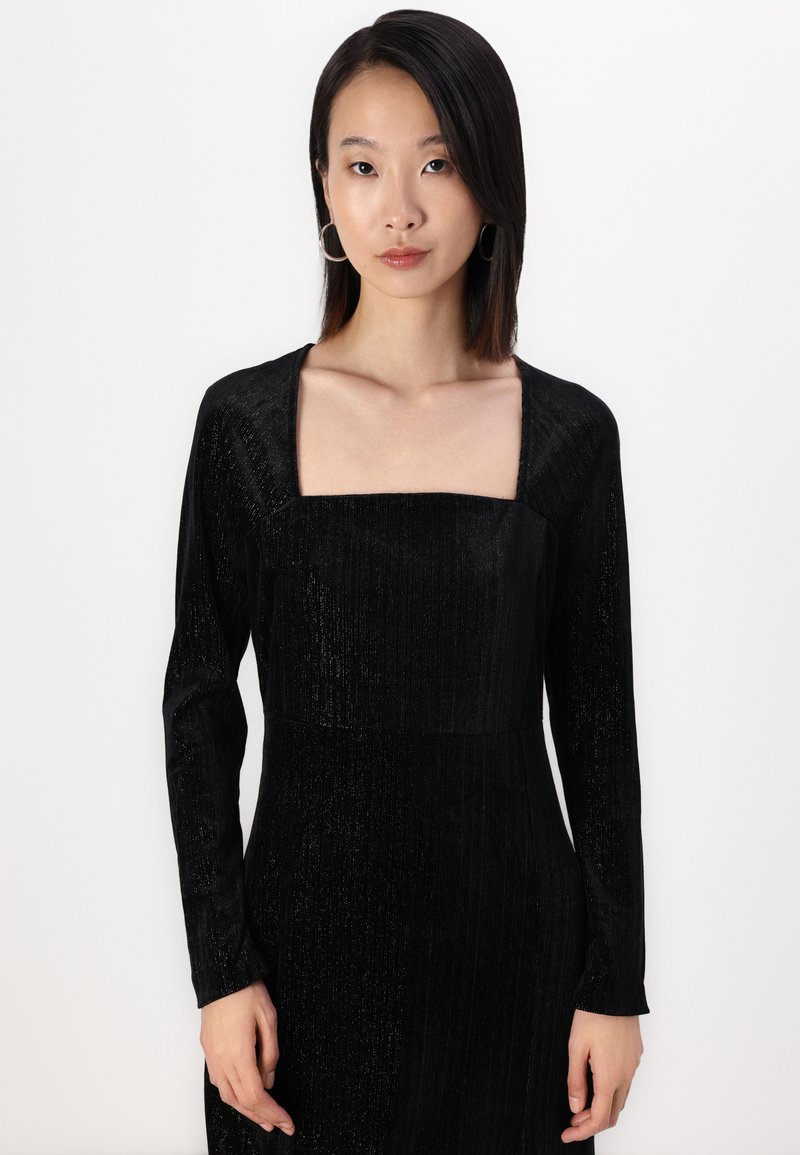 Schwarzes Langarmkleid mit quadratischem Ausschnitt, aus strukturiertem Stoff mit einem dezenten Glanz und vertikalen Rippungen.