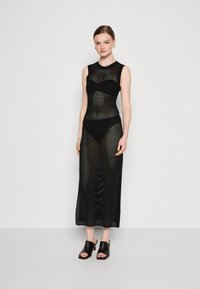 Rochie neagră din plasă cu design fără mâneci, având un guler înalt și o fustă lungă, transparentă. Purtați-o peste un costum de baie negru, asortată cu sandale chunky negre.