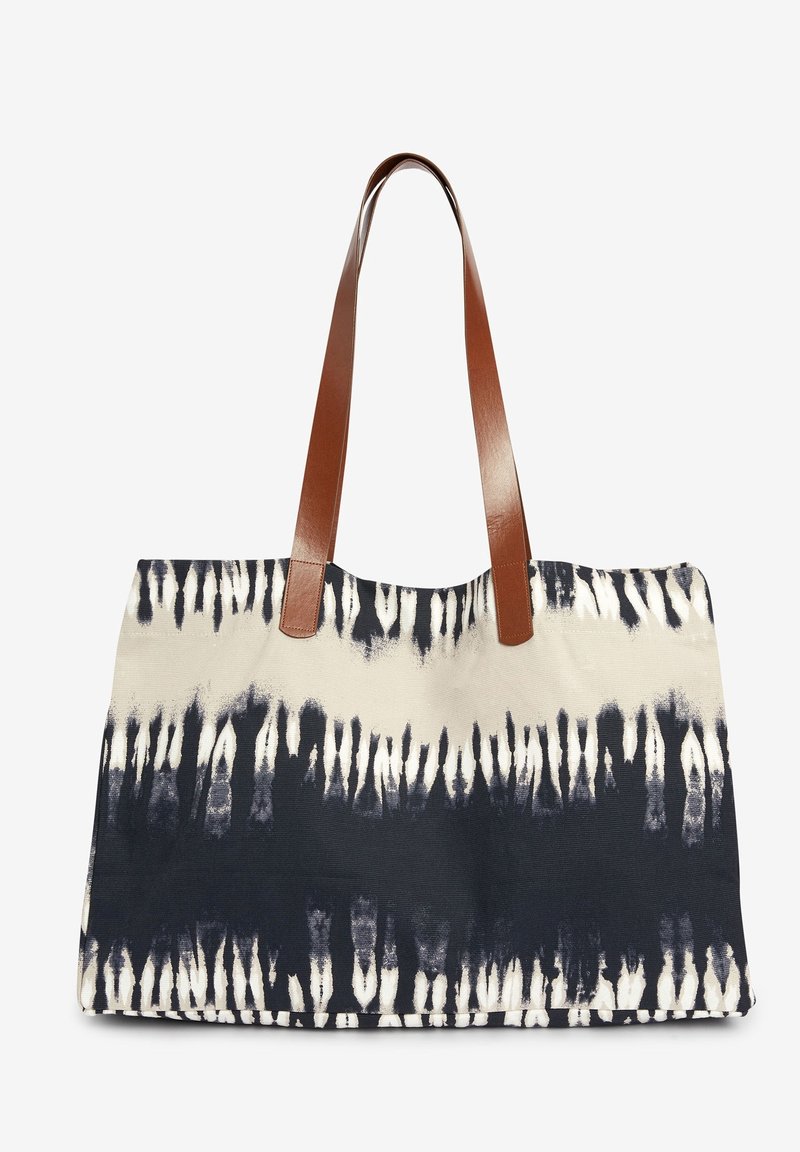 Sac en toile présentant un motif tie-dye bleu marine et crème avec deux anses en cuir marron. Conception rectangulaire robuste avec une surface texturée.