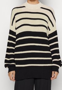 Pull en maille présentant des rayures horizontales noires et crème, col rond, manches longues avec poignets et ourlet côtelés.