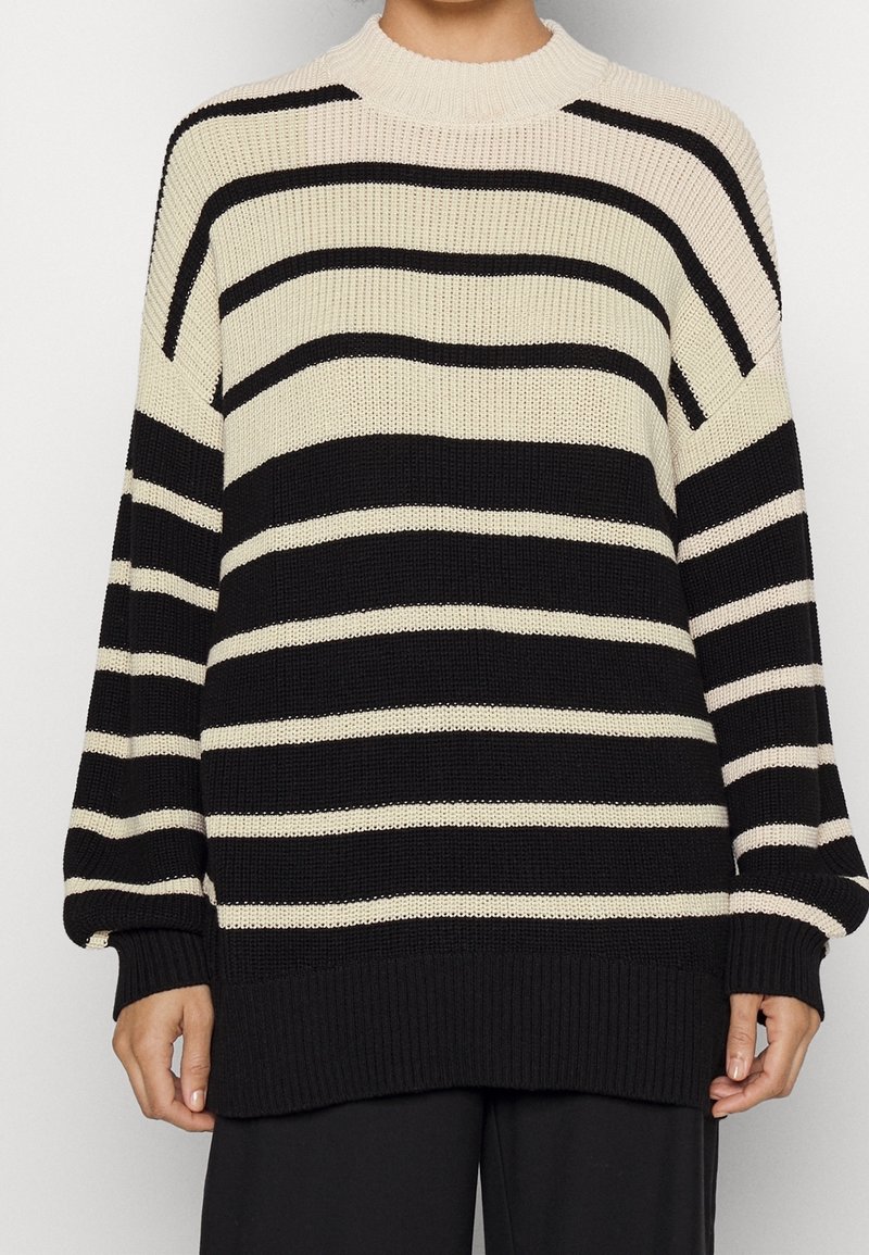 Pull en maille présentant des rayures horizontales noires et crème, col rond, manches longues avec poignets et ourlet côtelés.