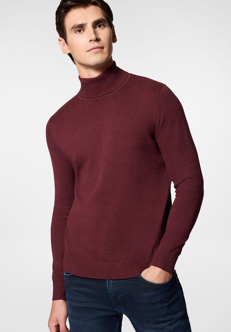 Burgundowy sweter z golfem o dopasowanym kroju, z prążkowanymi mankietami i dołem oraz gładką teksturą, w zestawie z ciemnymi dżinsami.