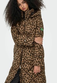 Pikowana kurtka z kapturem w panterkę, w odcieniach brązu i beżu, z przeszyciami, zapinana na zamek, z zieloną naszywką z logo na rękawie.