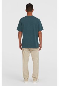 Teal bomulds T-shirt med korte ærmer og rund hals, parret med beige lige ben bukser og hvide sneakers. Enkelt design, ingen mønstre.