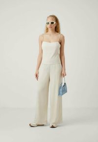 White tank top with thin straps, wide cream pants, light blue bag, and oversized white sunglasses. Smooth texture and relaxed fit.