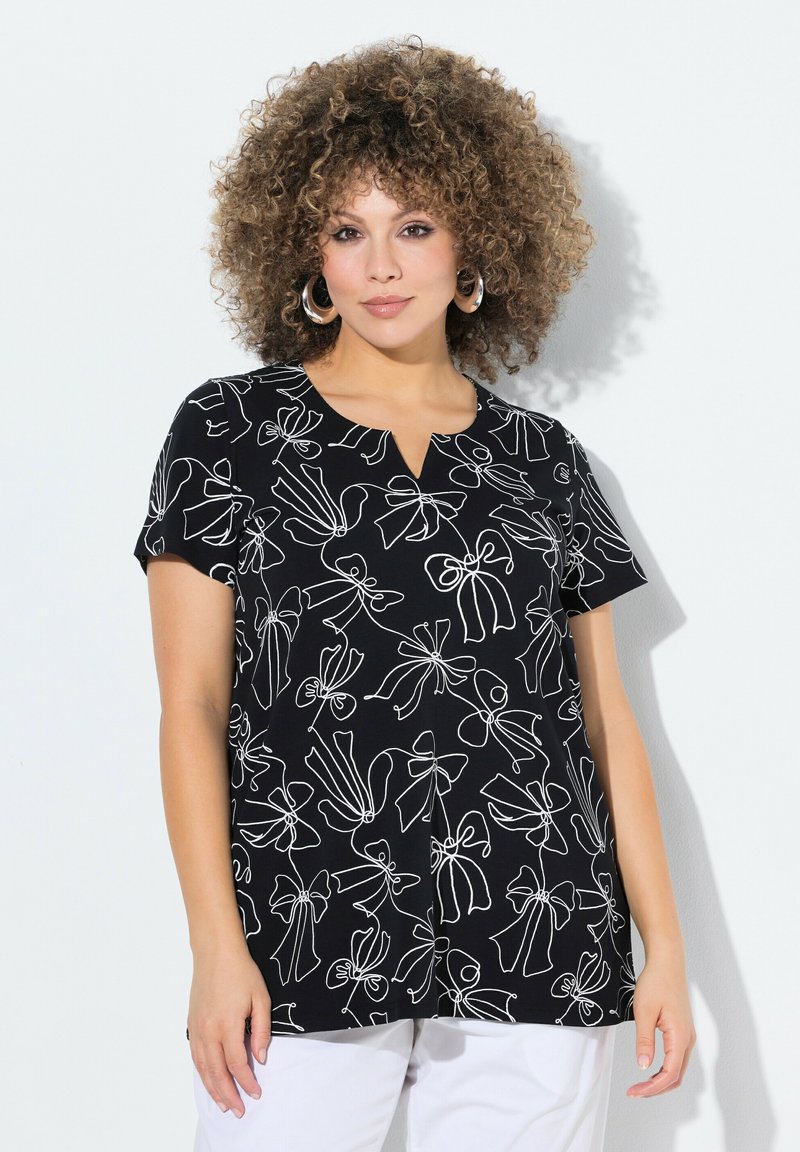 Top negro de manga corta con un patrón de lazo blanco y diseño de escote en V. Fabricado en un material suave, con un ajuste relajado y bajo curvado.