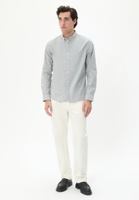 Lichtgrijs button-up shirt met lange mouwen, witte broek en zwarte instapschoenen. Het shirt heeft een klassieke kraag en een zachte stoftextuur.