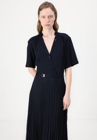 Navy dress with a deep v-neck, short sleeves, button details, and a fitted waist, featuring a pleated skirt and a silver buckle accent.
