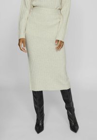 Falda midi de punto acanalado en beige claro combinada con botas altas negras ajustadas, con una textura suave y una silueta ajustada.