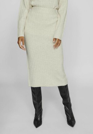 Falda midi de punto acanalado en beige claro combinada con botas altas negras ajustadas, con una textura suave y una silueta ajustada.