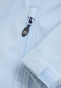 Tessuto blu chiaro con texture liscia, dotato di una cerniera e una chiusura in Velcro. Cursore della cerniera nero con dettagli del logo.