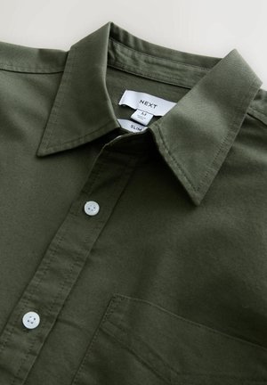 Oliwkowa koszula slim-fit z wyraźnym kołnierzykiem, białymi guzikami i kieszonką; wykonana z gładkiego materiału z detalami szycia.