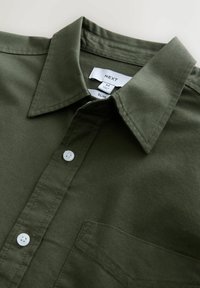 Chemise ajustée olive avec un col structuré, des boutons blancs et une poche ; fabriquée en tissu lisse avec des détails de couture.
