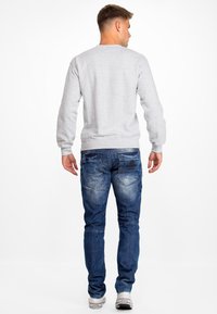 Sweatshirt gris avec des poignets et un ourlet côtelés, associé à un jean en denim bleu présentant des détails décolorés et des poches arrière avec des coutures visibles.
