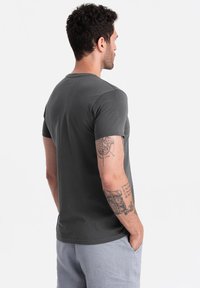 Szara krótka koszulka z krótkim rękawem, wykonana z miękkiej bawełny, z okrągłym dekoltem i klasycznym fasonem. Widok z tyłu ukazuje gładką fakturę i czyste linie.