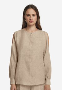 Beige Leinenbluse mit kalten Schultern, rundem Ausschnitt und Knopfverschluss vorne. Lange Ärmel mit Manschettendetail. Weiche Textur.