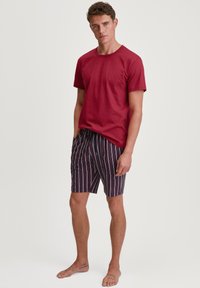 Rode katoenen t-shirt gecombineerd met marineblauwe korte broek met verticale strepen in roze en wit. De korte broek heeft een elastische tailleband.
