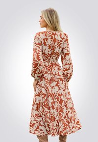 Kleid mit Blumenmuster in rostorangefarbener Hintergrund und weißen Akzenten, mit langen puffärmel und gestuftem Saum.