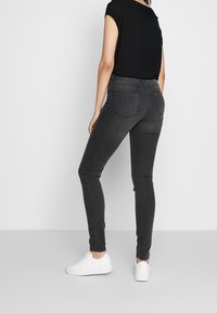 Jeans ajustados de color gris oscuro hechos de denim, con una cintura de altura media, diseño de cinco bolsillos y ligeros detalles de desgaste. Se llevan con una camiseta negra y zapatillas blancas.