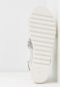 Semelle de sandale blanche avec des rainures horizontales, taille 37, et le nom de la marque "GUESS" embossé, photographiée sur un fond d'angle blanc.
