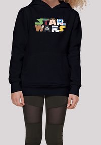 Sudadera negra con un gráfico multicolor de "STAR WARS". Tejido suave, bolsillo frontal, puños y dobladillo acanalados. Combinada con leggins oscuros.