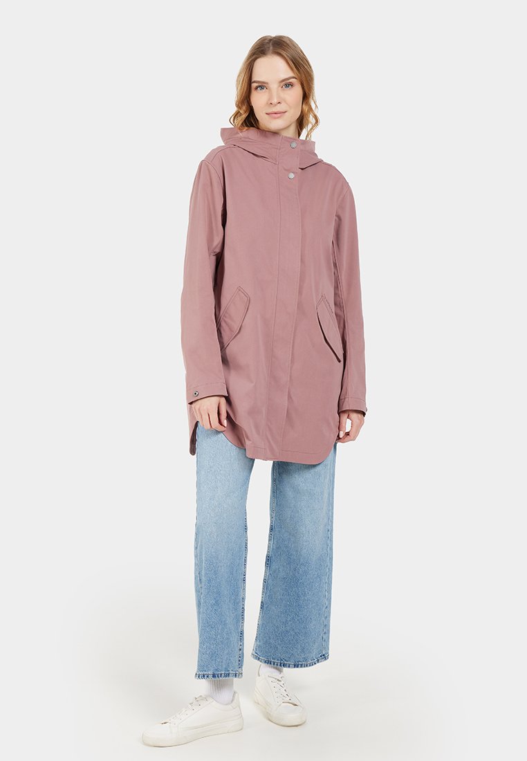 Helle rosa wasserdichte Jacke mit Kapuze, Druckknopfverschluss auf der Vorderseite und zwei seitlichen Taschen, kombiniert mit blauen weit geschnittenen Jeans und weißen Turnschuhen.