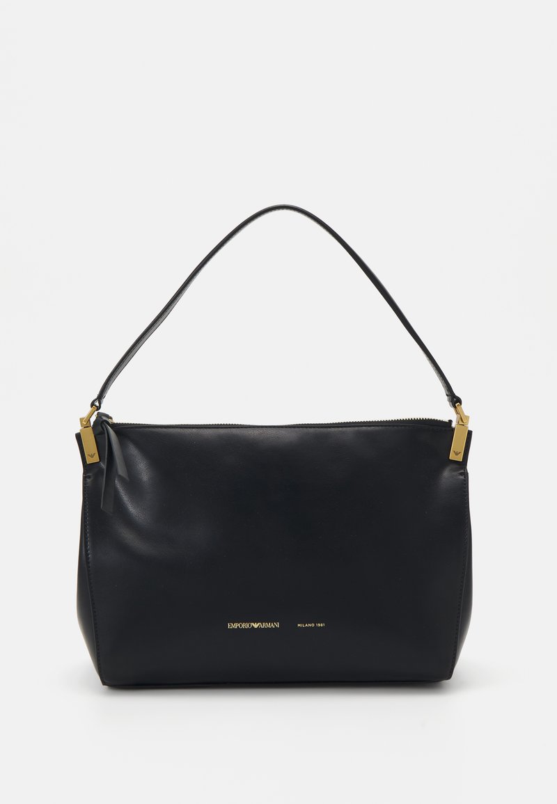 Melnas ādas rokassomiņa ar rāvējslēdzēja aizdari, izliekto rokturi un zelta toņa furnitūru. Iepriekšējo zīmējumu minimāla zīmola atzīme zeltā uz priekšpuses.