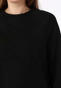 Sudadera negra con cuello de canalé, textura suave, mangas raglán y un diseño simple, adecuada para un uso casual.