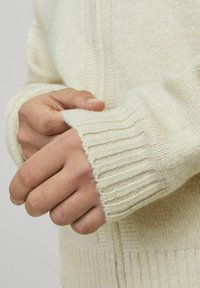 Cremfarbener Strickpullover mit gerippten Bündchen und strukturiertem Detail an der Vorderseite, aus weichem Wollmaterial mit lockerer Passform.