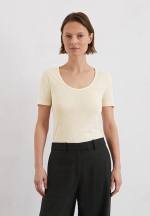 Light yellow short-sleeve shirt with a scoop neckline, soft texture, worn with dark pants, creating a two-tone outfit. Simple design.