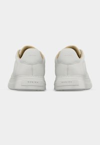 Ζευγάρι λευκά αθλητικά παπούτσια χαμηλού ύφους με μπεζ εσωτερική επένδυση, εμφανιζόμενα από πίσω, με σήμανση στο τακούνι και στη σόλα.