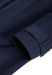 Rękaw granatowego płaszcza z paskiem i brązowym guzikiem na mankiecie, pokazujący fakturę tkaniny i szwy.