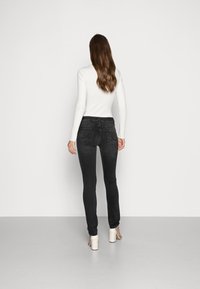 Jeans justos pretos com bolsos traseiros, combinados com uma blusa branca de manga longa canelada, usados com sandálias de salto de cor clara.