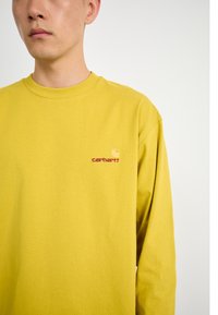 Long-sleeve yellow t-shirt made of soft cotton, featuring a small red Carhartt logo on the left chest. Simple crew neckline and relaxed fit.