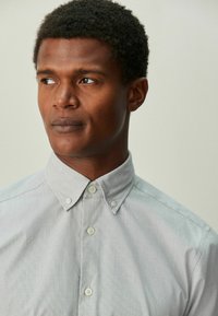 Hellgraues gewebtes Hemd mit Button-Down-Kragen, das eine subtile Struktur und drei Knöpfe vorne aufweist.