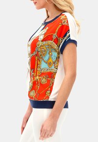 Bluzka z krótkim rękawem z dekoracyjnym nadrukiem w pomarańczowe i niebieskie wzory, z granatowym ściągaczem u dołu i białymi rękawami, wykonana z gładkiego materiału.