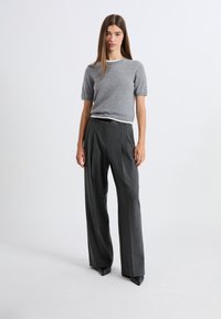 Szary sweter z krótkim rękawem z kontrastującym dekoltem, zestawiony z wysokim stanem ciemnoszarych plisowanych spodni i czarnych szpiczastych szpilek.