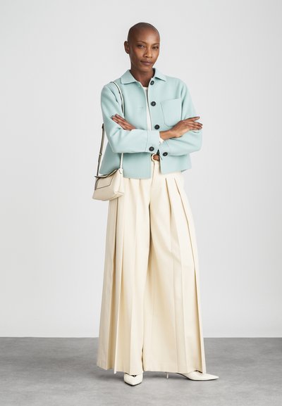 Zkrácená mintově zelená bunda, černé knoflíky, bílá košile pod ní a široké béžové kalhoty, doplněné bílými botami na podpatku s špičatou špičkou a malou taškou.