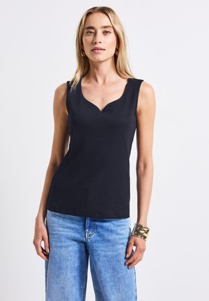 Top nero senza maniche con scollatura a scallop, realizzato in tessuto a costine. Abbinato a jeans a gamba larga azzurri e un bracciale in oro massiccio.