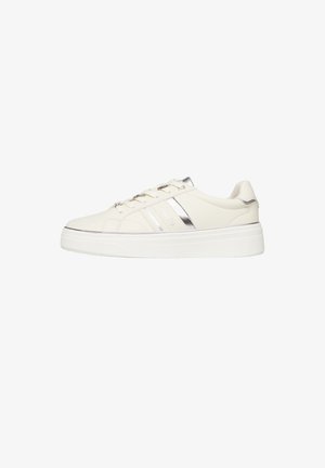 Białe, niskie trampki z grubą podeszwą, srebrnym paskiem oraz metalicznymi akcentami na oczkach sznurowadeł i języku buta.