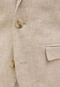 Blazer de lino beige con tejido texturizado, tres botones delanteros y diseño clásico de solapa con un único bolsillo en el lado izquierdo.