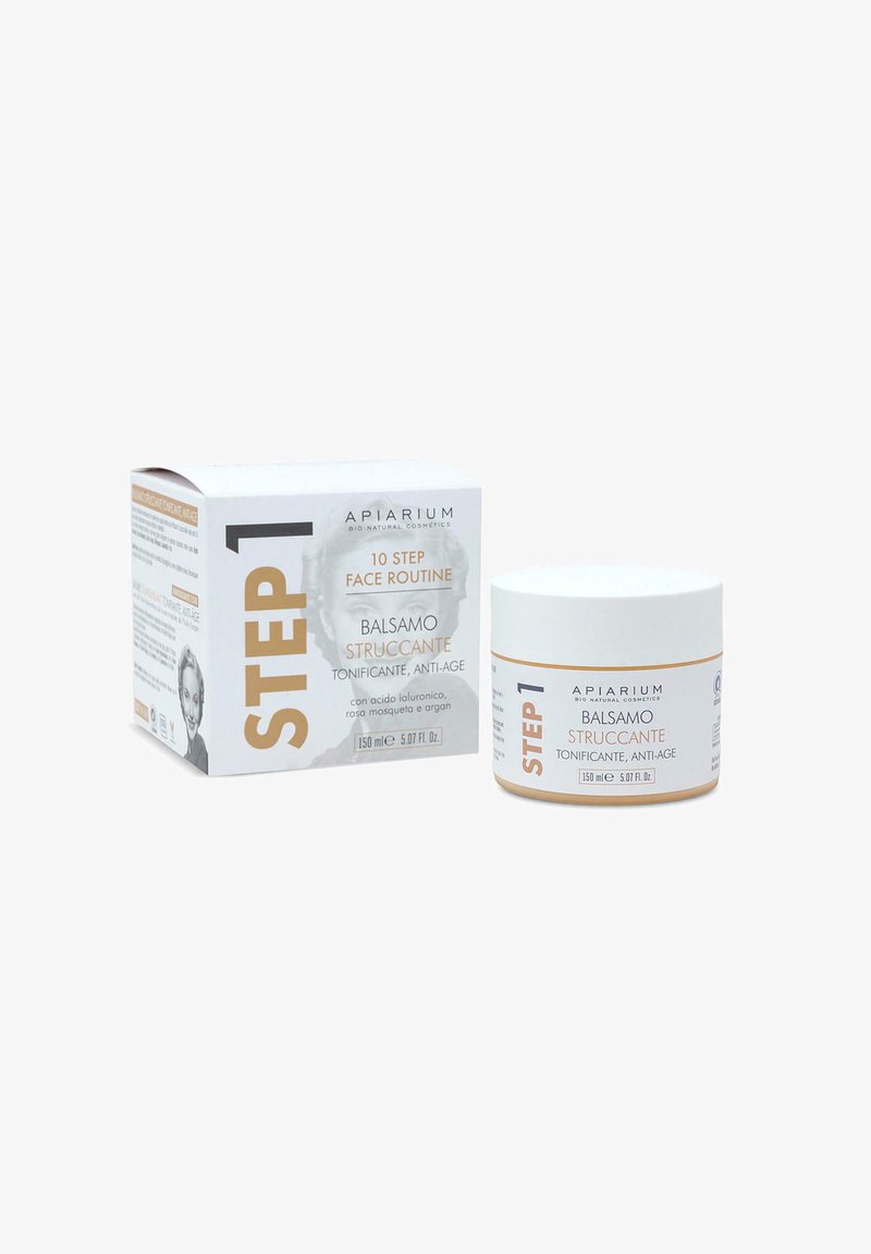 Crema struccante balsamo in un barattolo bianco con un accento dorato, posizionata accanto al suo packaging bianco caratterizzato da testo in grassetto e una grafica.