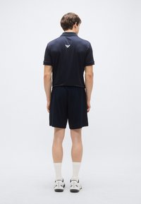 Námornícka modrá polokošeľa s krátkymi rukávmi a golierom, doplnená o zodpovedajúce krátke nohavice v rovnakom odtieni. Na zadnej strane je logo. Hladká textúra látky.