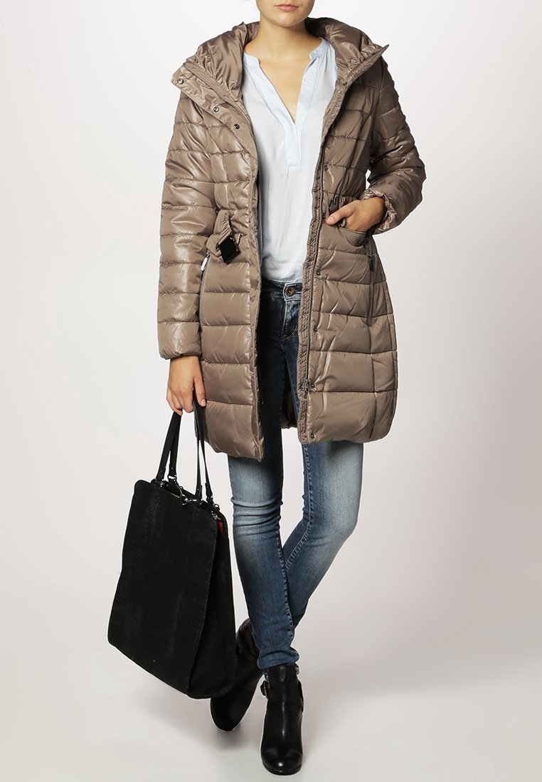 Beżowy, pikowany płaszcz z zamek błyskawicznym z przodu, kapturem i bocznymi kieszeniami, w połączeniu z jasnoniebieską koszulą, dżinsami i czarną torbą typu tote.