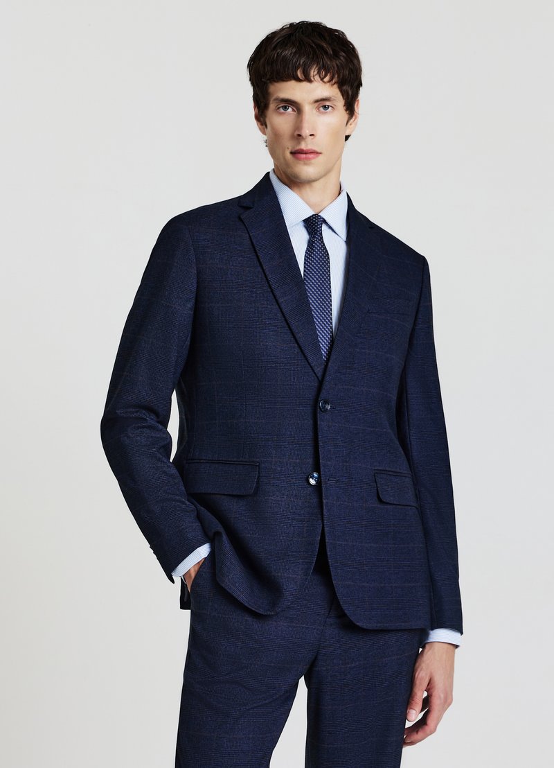 Completo blu navy con motivo a trama, caratterizzato da giacca monopetto, rever a lancia e due tasche frontali. Accompagnato da una camicia azzurro chiaro e una cravatta blu.